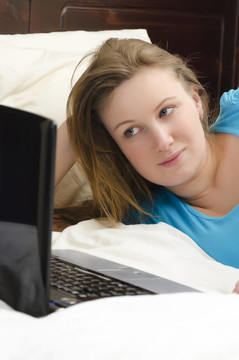 漂亮的女孩躺在床上看著筆記本電腦