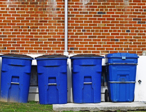 四个蓝色的塑料垃圾桶沿着草地的墙壁和一个混凝土平台为你的文本。