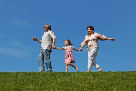 小女孩和她的祖父母在草地上奔跑，手牵着手
