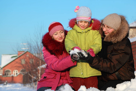 爸爸媽媽在冬天給女兒在戶外做雪球，爸爸媽媽坐在家里