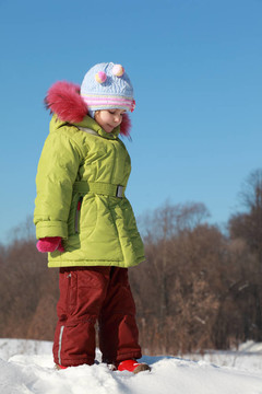 冬天里，穿著綠色夾克的小女孩站在雪地里，想；遠(yuǎn)處的樹