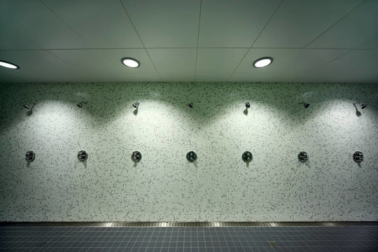 大；灯；空旷的公共淋浴房；墙壁上的绿色瓷砖；灰色地板
