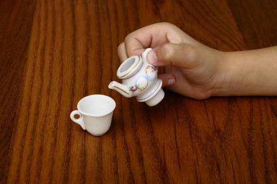 小孩用手在茶杯里倒茶