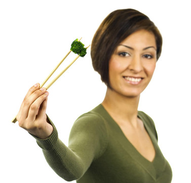 微笑女士用筷子盛著一片熟綠花椰菜。拍攝在2 eV的白色背景。