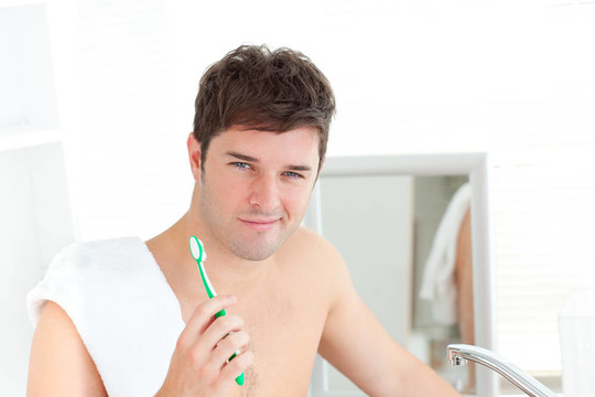 微笑的年轻人用毛巾在家里的浴室刷牙