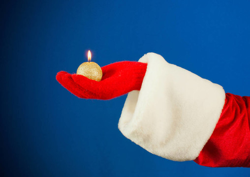 Santa手在藍色背景上手持燃燒的蠟燭
