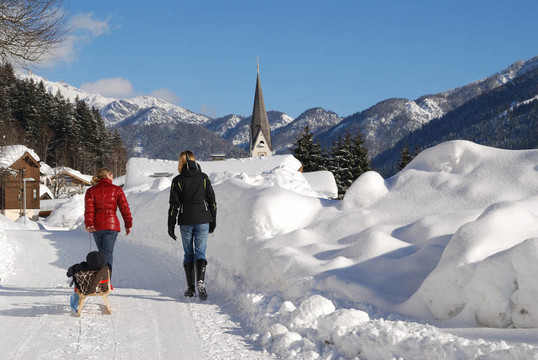 年輕女性嬰兒在雪橇走在白雪覆蓋的景觀在奧地利。