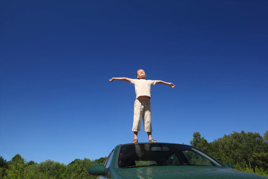 男孩站在汽車的頭上，抬起天空的臉，雙手放在一邊