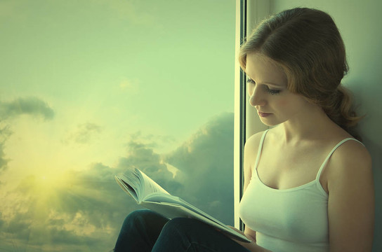 美麗的年輕女子坐在窗前，在夕陽下看書
