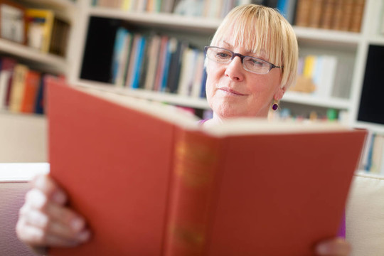 快樂的高級婦女在家里戴眼鏡看書