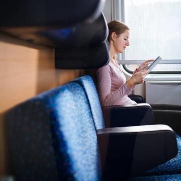 年輕女子坐火車旅行時使用平板電腦