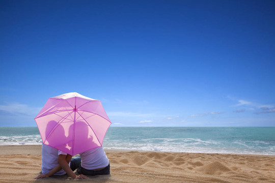 年輕情侶用雨傘在海灘浪漫接吻