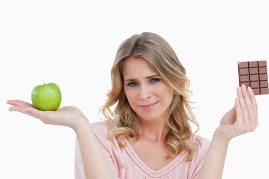 年輕的金發(fā)女人拿著一個(gè)蘋(píng)果和一塊巧克力