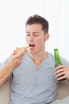 一個(gè)男人手里拿著一塊比薩餅和一些啤酒