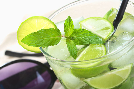 mojito雞尾酒由白色朗姆酒；冰塊；糖；薄荷葉和檸檬在后面的黑色吸管和太陽鏡（選擇性聚焦；對薄荷葉