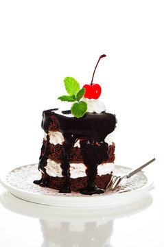 一个有2层白色奶油的小巧克力蛋糕；在白色背景上的樱桃和薄荷