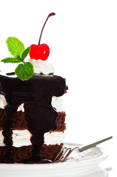 一个有2层白色奶油的小巧克力蛋糕；在白色背景上的樱桃和薄荷
