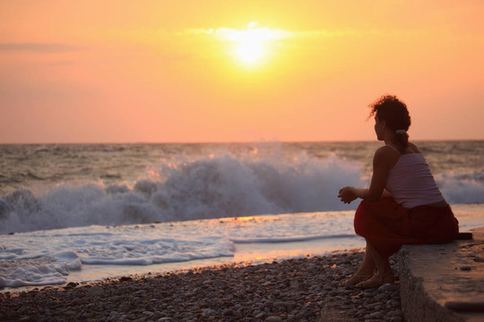 坐在夕陽波浪海灘上的年輕女子剪影