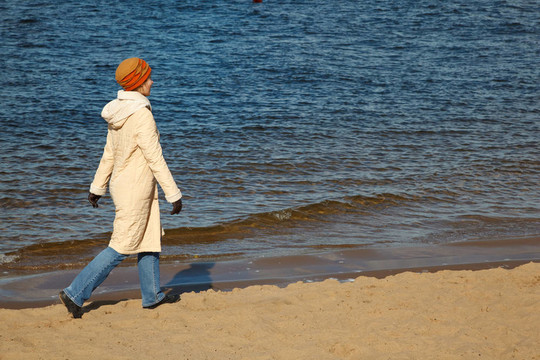 女孩走在秋天海滩上的帽子；外套；牛仔裤和运动鞋。