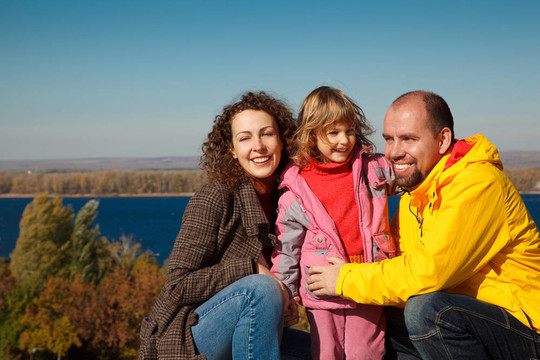 带着妈妈和爸爸的小女孩；在明亮的秋日。自然幸福家庭。