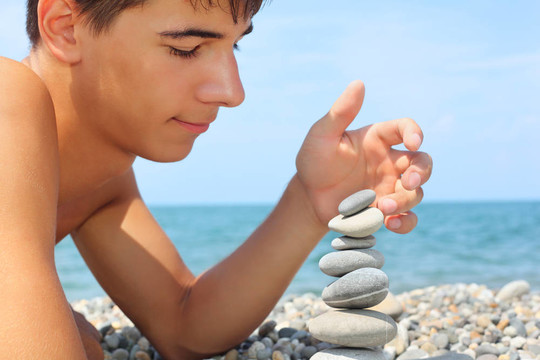 十几岁的男孩躺在石海岸；创造金字塔从卵石