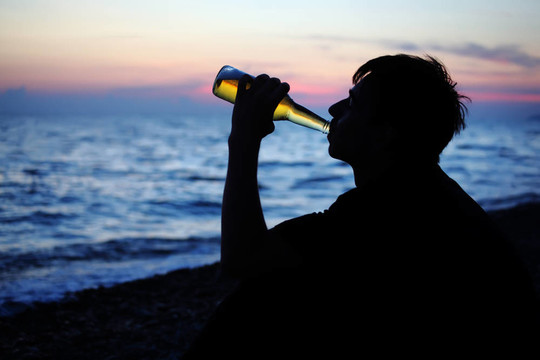 剪影少年男孩喝啤酒石海岸的夜晚