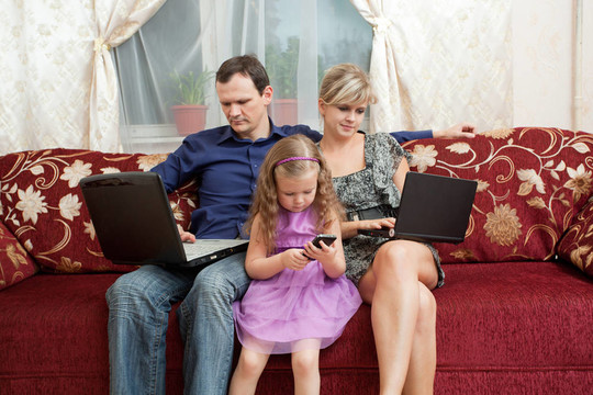 三口之家坐在沙发上，每人都有自己的电脑