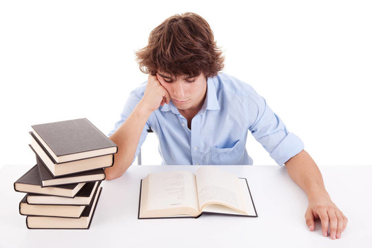 可愛的男孩在他的書桌上學(xué)習(xí)和閱讀一本書；白色的孤立的