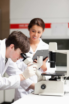 一个理科学生在显微镜下看着他的同学在实验室里写的照片