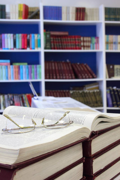 在圖書館書架的背景打開的書和眼鏡