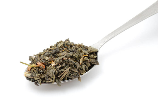 在白色背景上分離的金屬匙中的干綠茶