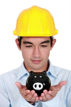 年輕的建筑工人手里拿著存錢(qián)罐