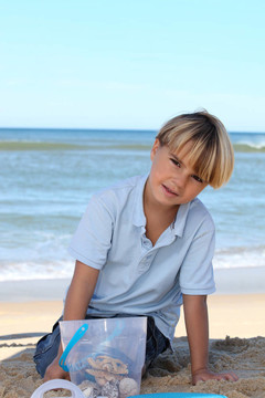 小男孩在海滩上的桶里收集海星