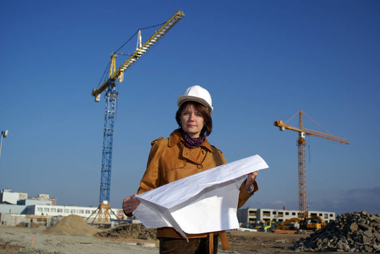 漂亮的女建筑師手持藍圖，站在建筑工地