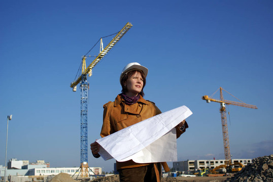 漂亮的女建筑師手持藍圖，站在建筑工地