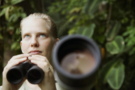 美丽的女人在雨林中用望远镜
