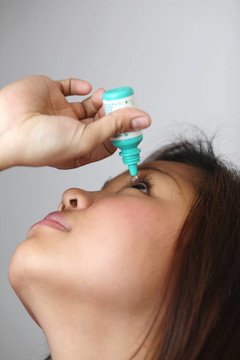 年輕的女人用眼藥水。
