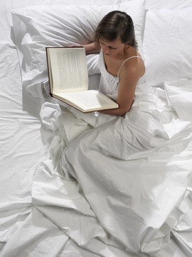一個漂亮的年輕女人在床上看書