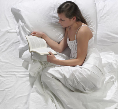 一個漂亮的年輕女人在床上看書