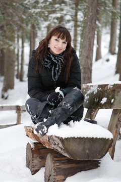 年輕女子坐在長凳上的白雪皚皚的森林