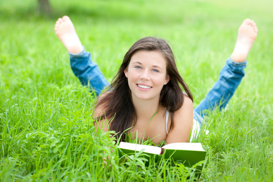 年輕漂亮的女孩正在草地上讀書(shū)