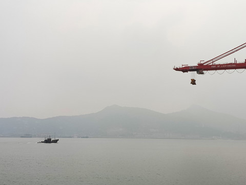 一艘漁船從港口集裝箱碼頭駛過