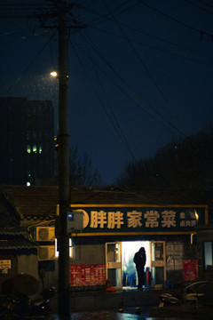 路燈下有人走出雨中的小飯館