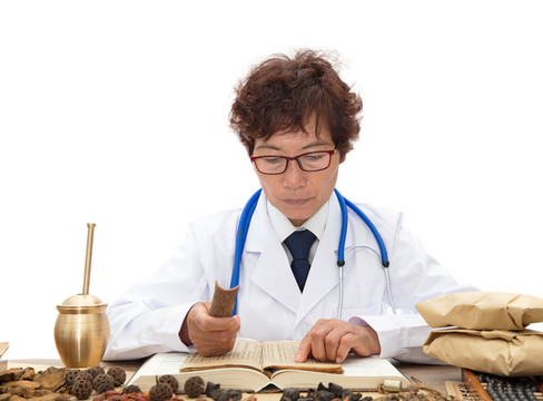老中醫(yī)拿著一塊桂皮翻看中藥典籍