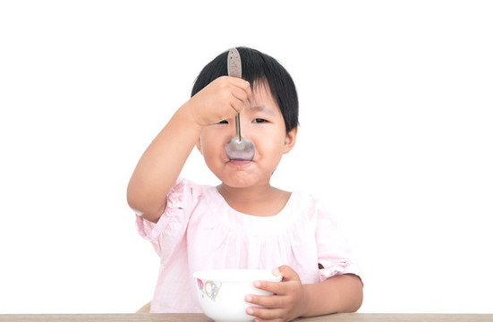 白背景前自立的孩子正在自己吃飯