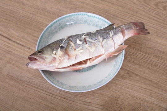 盤子里放著一條正在腌制的鱸魚