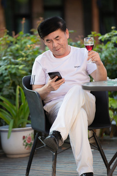 老年人在戶外坐著喝紅酒刷手機