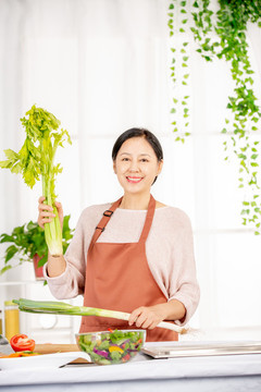 手拿芹菜在廚房做飯的中老年女性