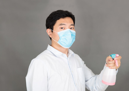 戴著口罩手拿消毒液噴灑的男士