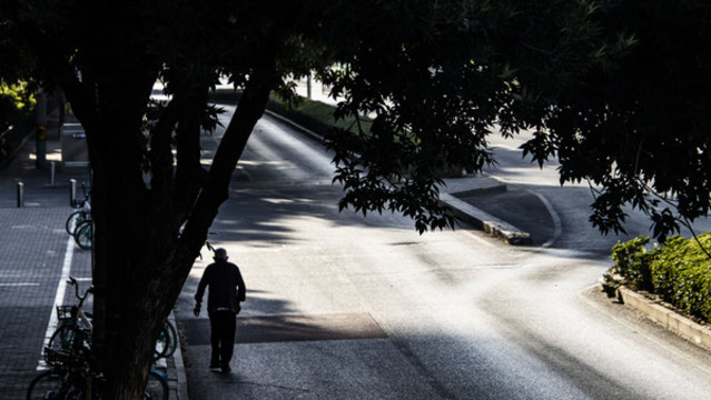 清晨在道路樹蔭下走路的老人